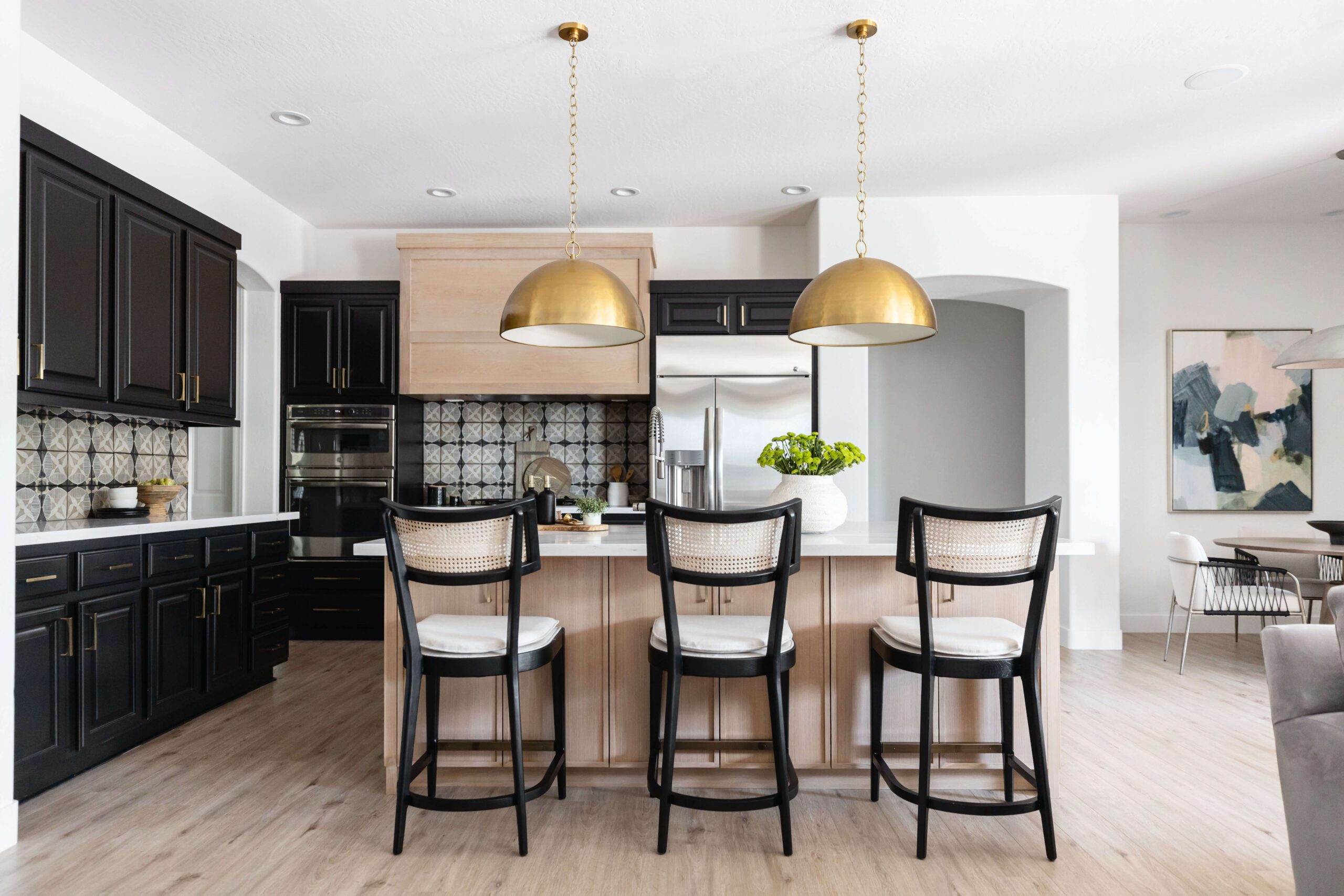 A kitchen with black cabinetry, brass pendant lights, a wood island, and cane-back barstools. — Living with Lolo. A kitchen with black cabinetry, brass pendant lights, a wood island, and cane-back barstools. — Living with Lolo.