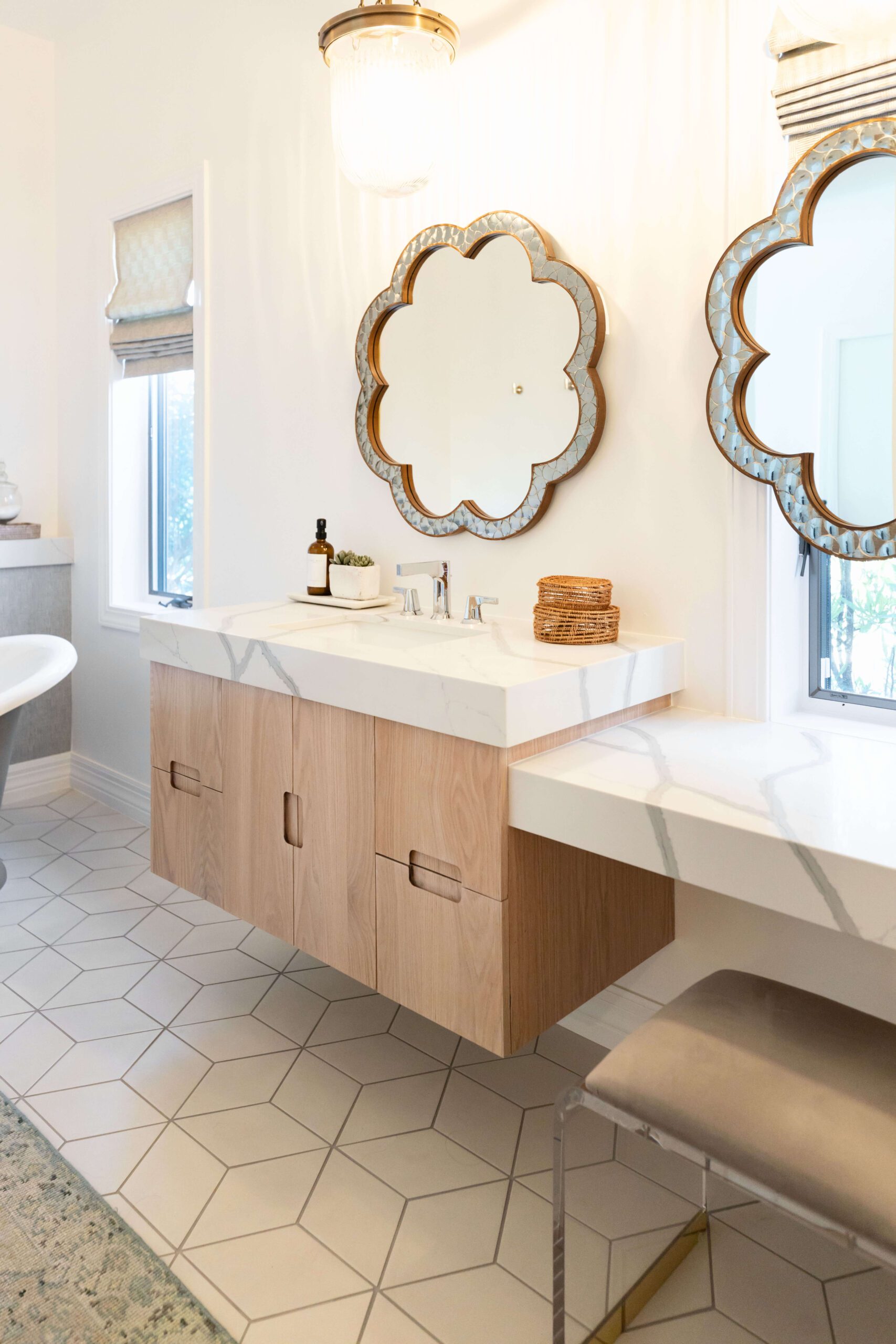 Bathroom with a floating wood vanity, marble countertop, mirrors, patterned floor tiles, and a cushioned stool. — Living with Lolo. Bathroom with a floating wood vanity, marble countertop, mirrors, patterned floor tiles, and a cushioned stool. — Living with Lolo.