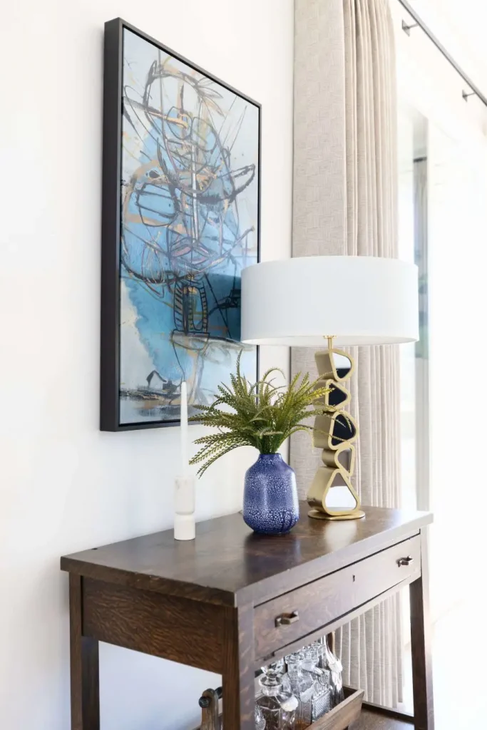 Close-up of dark wood console table with gold lamp, blue vase, and abstract wall art