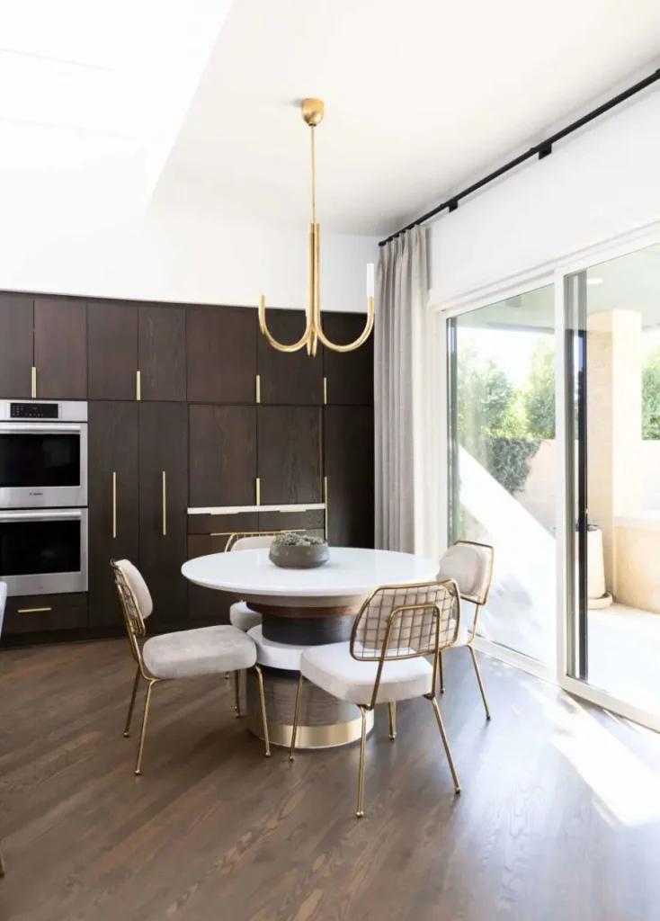 Bright dining room with white round table, gold-framed chairs, and dark wood cabinets