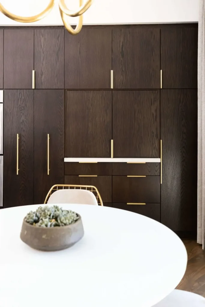 Dark wood kitchen cabinets with gold handles and a white round table in foreground