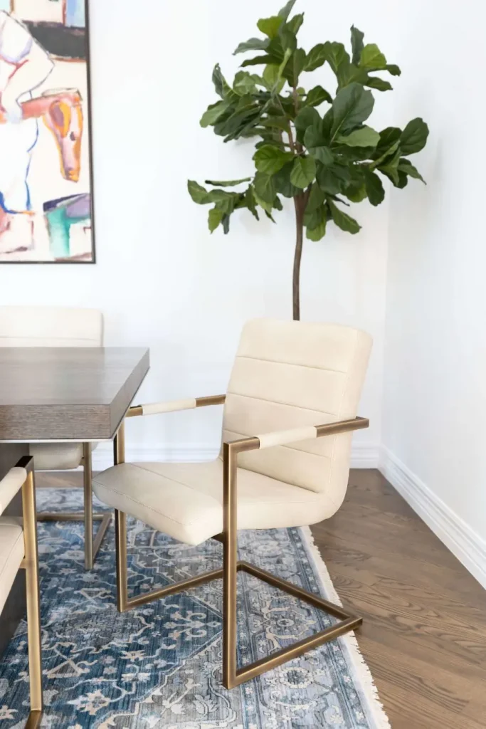 Close-up of beige cushioned dining chair with gold metal frame on patterned rug