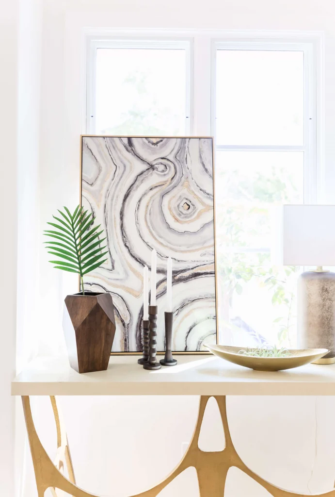 Decorative console table with geometric wood vase, candles, abstract art, and lamp
