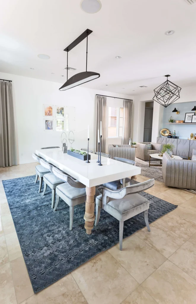 Modern dining and living area with white table, gray velvet chairs, and geometric lighting