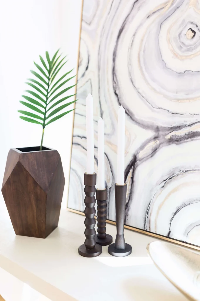 Wooden candleholders and geometric vase with palm leaf in front of abstract artwork