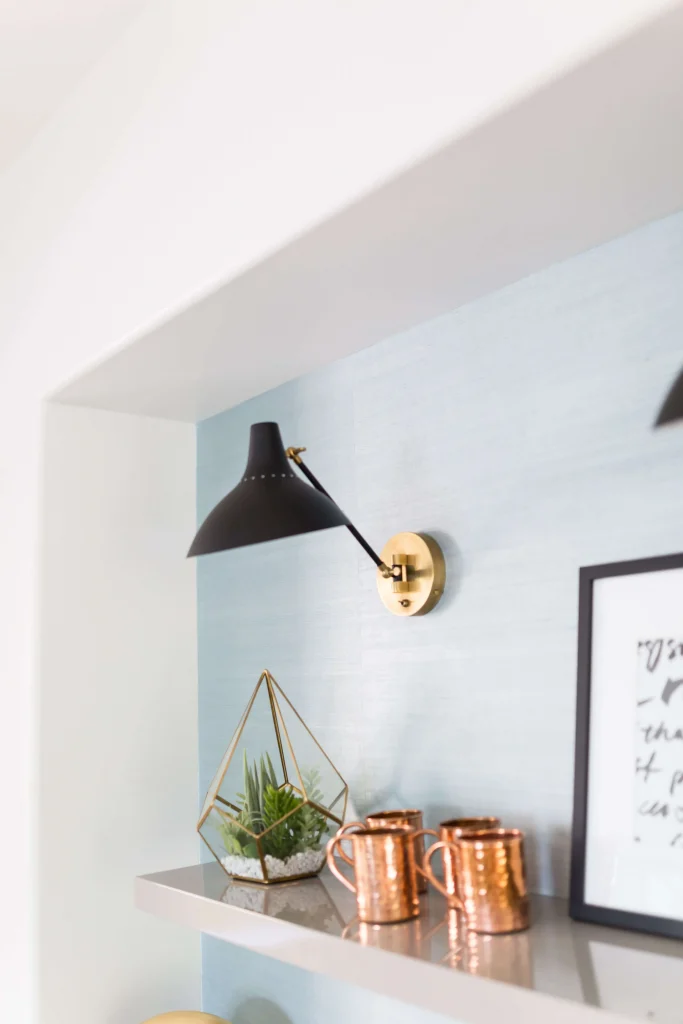 Copper mugs and glass terrarium with plants under black sconce light