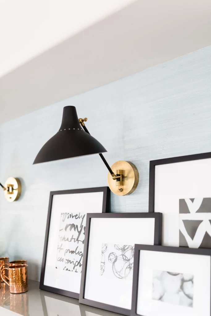 Black-framed art prints on shelf under black and brass sconce lights
