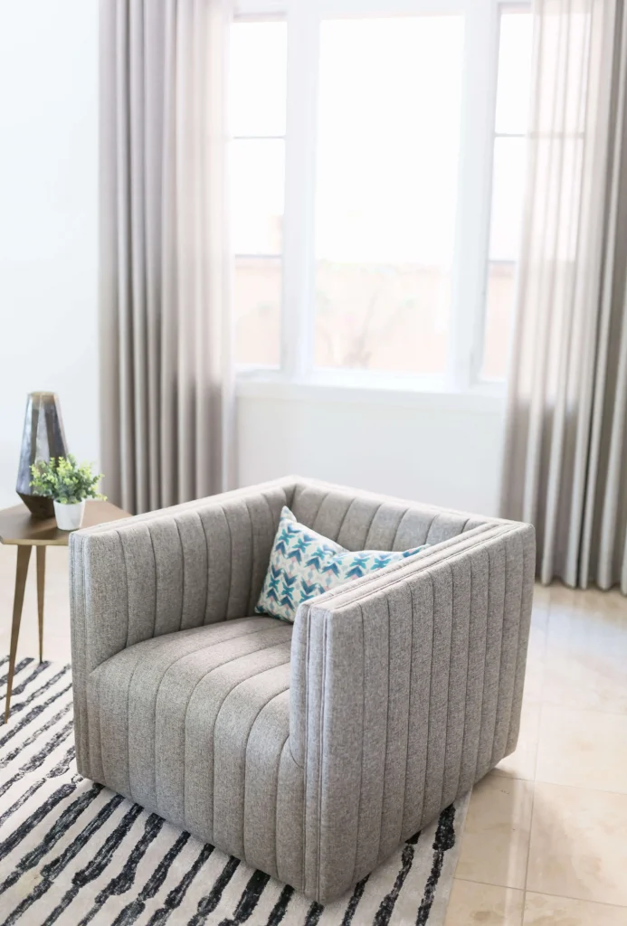 Grey upholstered armchair with patterned pillow in a bright living space