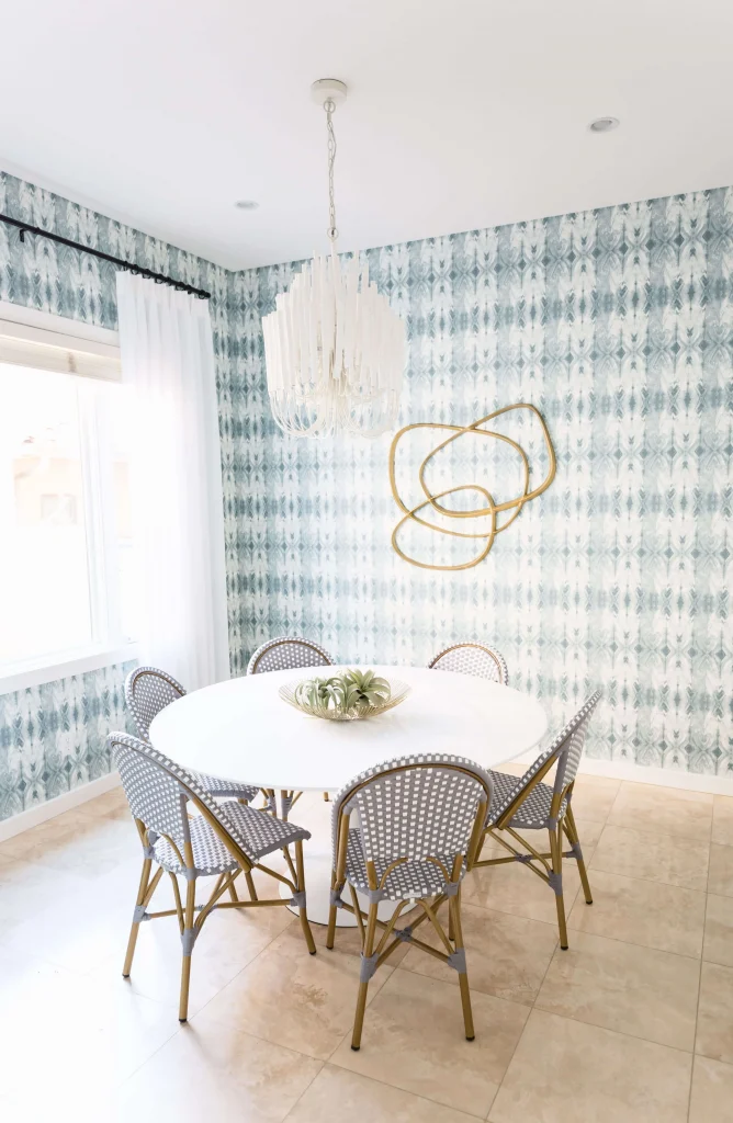 Round white dining table surrounded by six gray and white woven chairs in a bright room