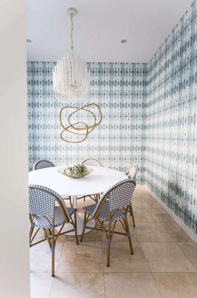 Side view of a round white dining table surrounded by six gray and white woven chairs in a bright room