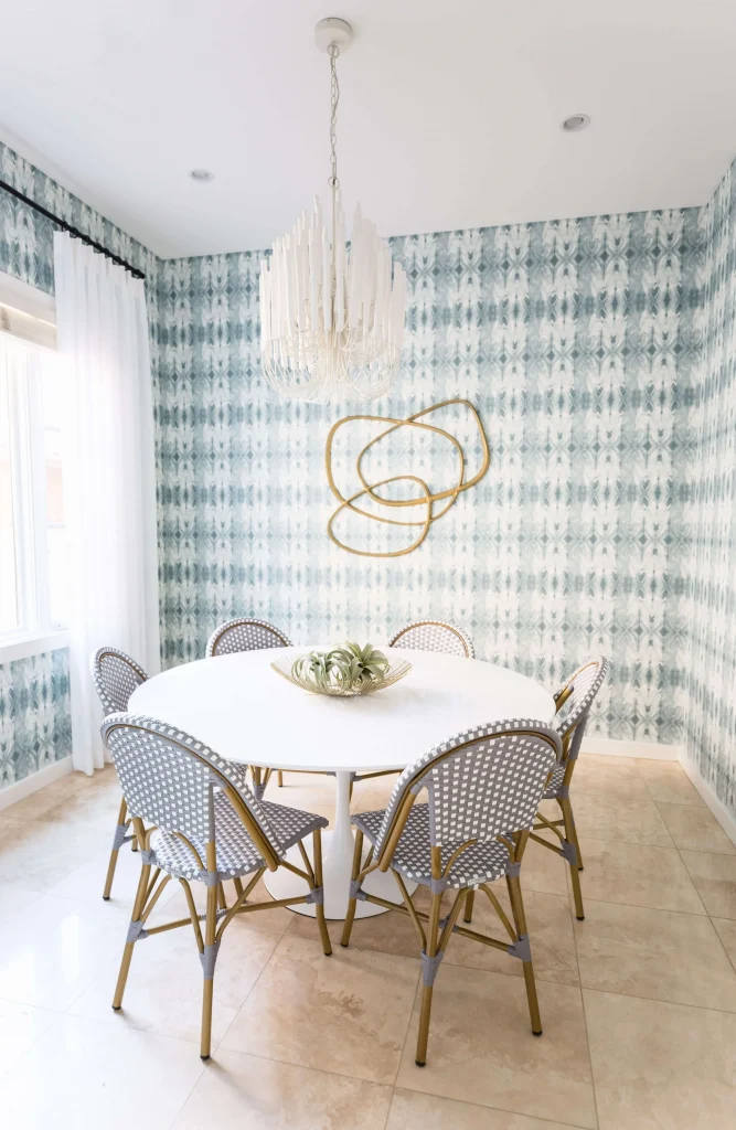 Dining room with round white table and six woven chairs under a white chandelier
