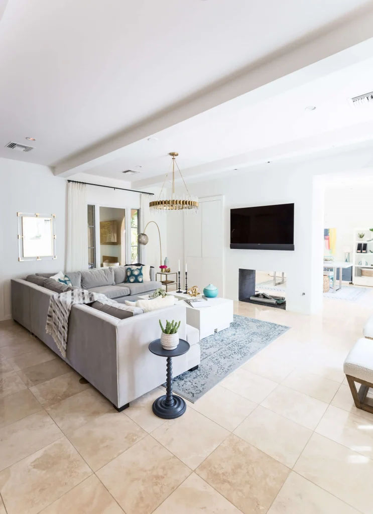 Bright modern living room with large gray sectional sofa, black pedestal side table with succulent, blue patterned rug, and wall-mounted TV.