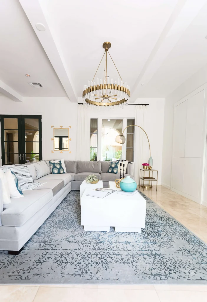Bright living room with light gray sectional sofa, white coffee tables, and gold chandelier.