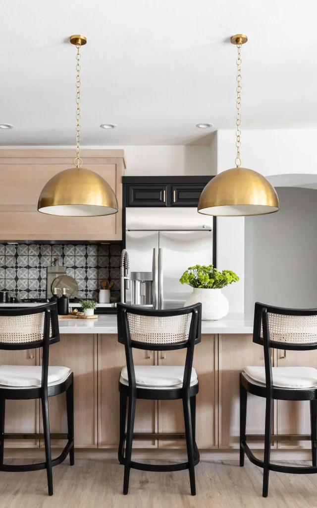 Kitchen island with three black chairs and brass pendant lights