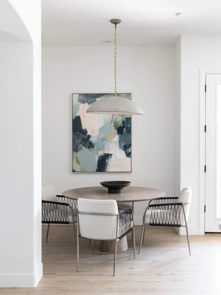 Minimalist dining space with round wooden table, modern chairs, and abstract wall art