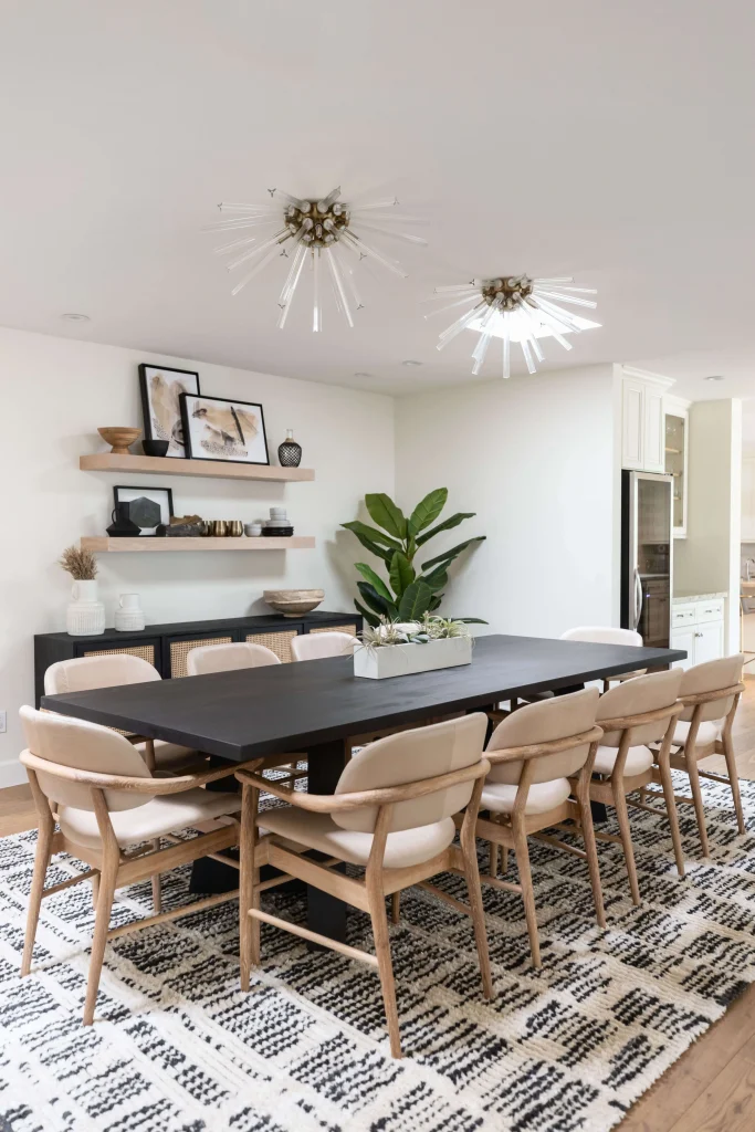 Dining room with long table, neutral chairs, and open shelves