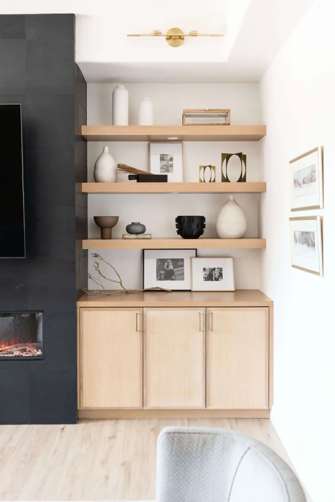 Wooden floating shelves with decorative items and framed photos next to a black tiled fireplace