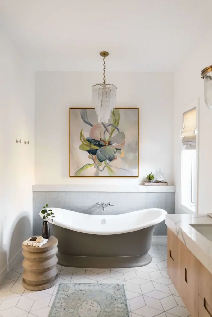 Modern bathroom featuring a freestanding gray and white bathtub, abstract painting, and wooden side table.