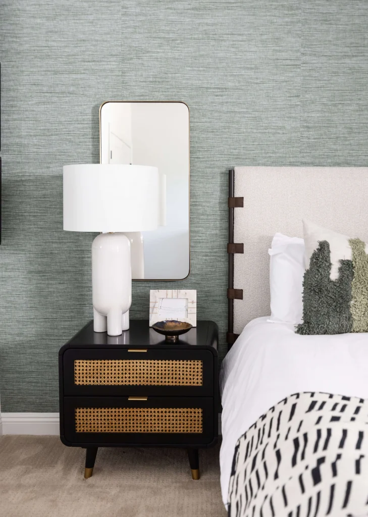 Bedside table with rattan drawers, white lamp, and mirror