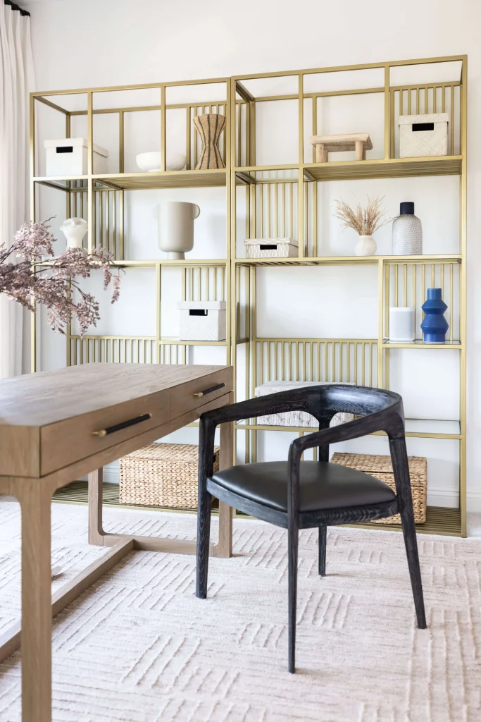Office corner with wood desk, black chair, and brass shelves