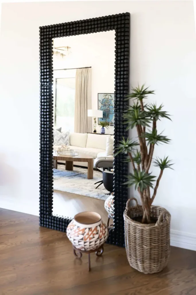 Large floor mirror reflecting living room with sofa and coffee table