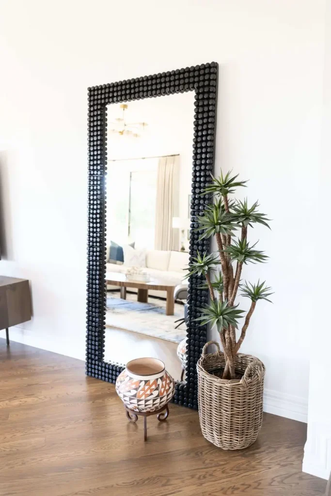 Black framed mirror with round bead texture beside a tall indoor plant in wicker basket