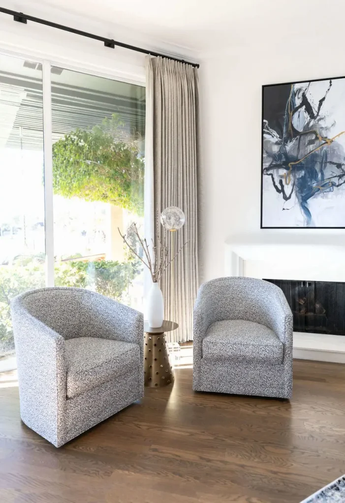 Pair of barrel chairs by sliding glass door with beige curtains and decorative side table