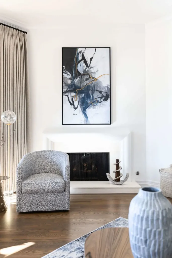 Single gray and white patterned barrel chair near white fireplace with abstract art above