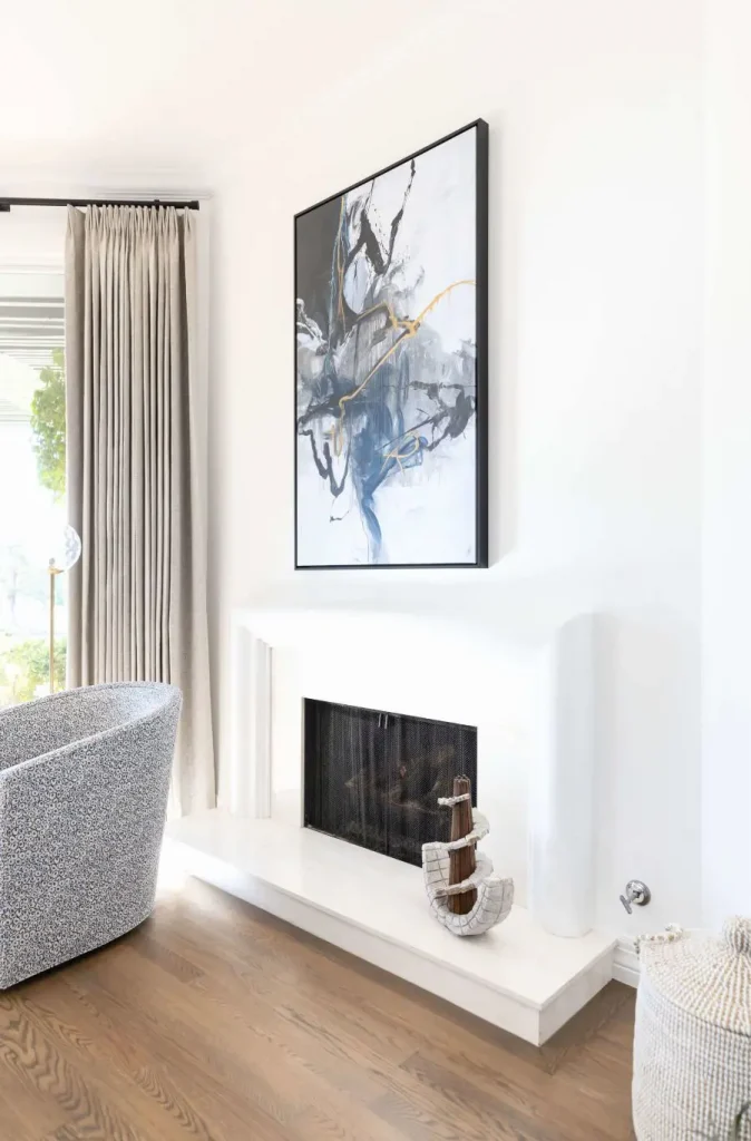 Minimalist fireplace with abstract painting above and textured swivel chair