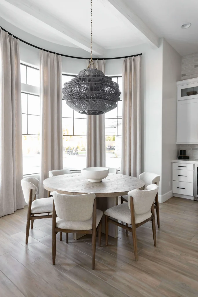 Round wooden table with white chairs by windows