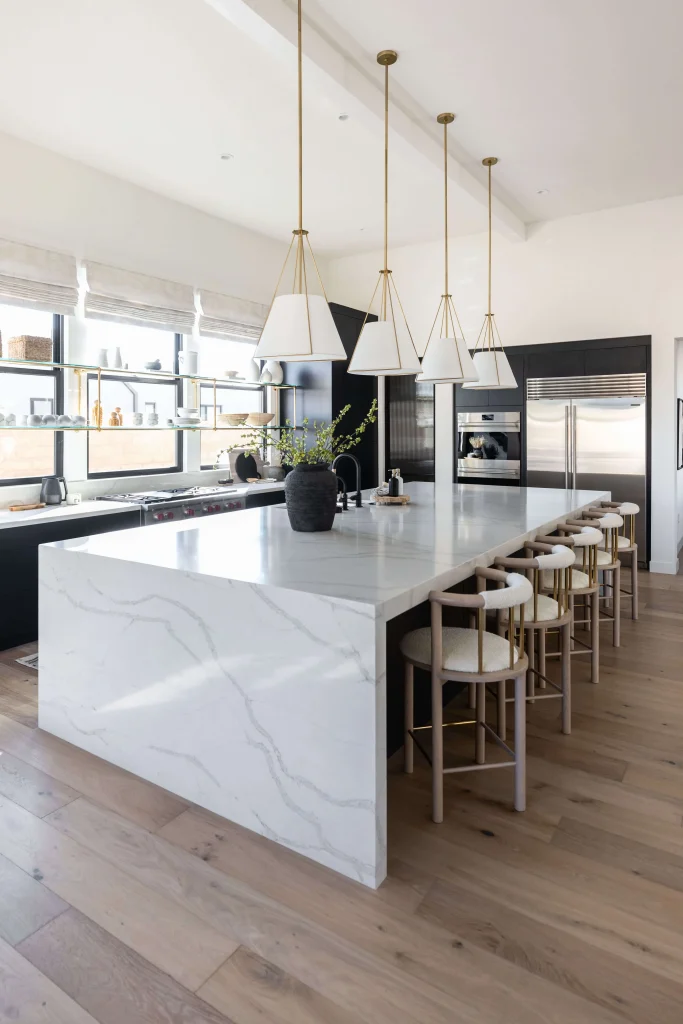 White waterfall kitchen island with gold pendant lights and bar stools