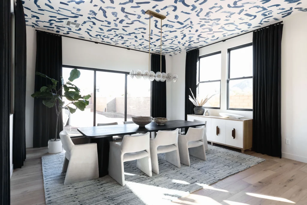 Dining table under bold patterned ceiling with black curtains
