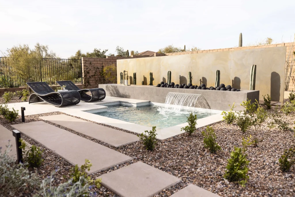 Backyard pool with waterfall feature, desert plants, and lounge seating.