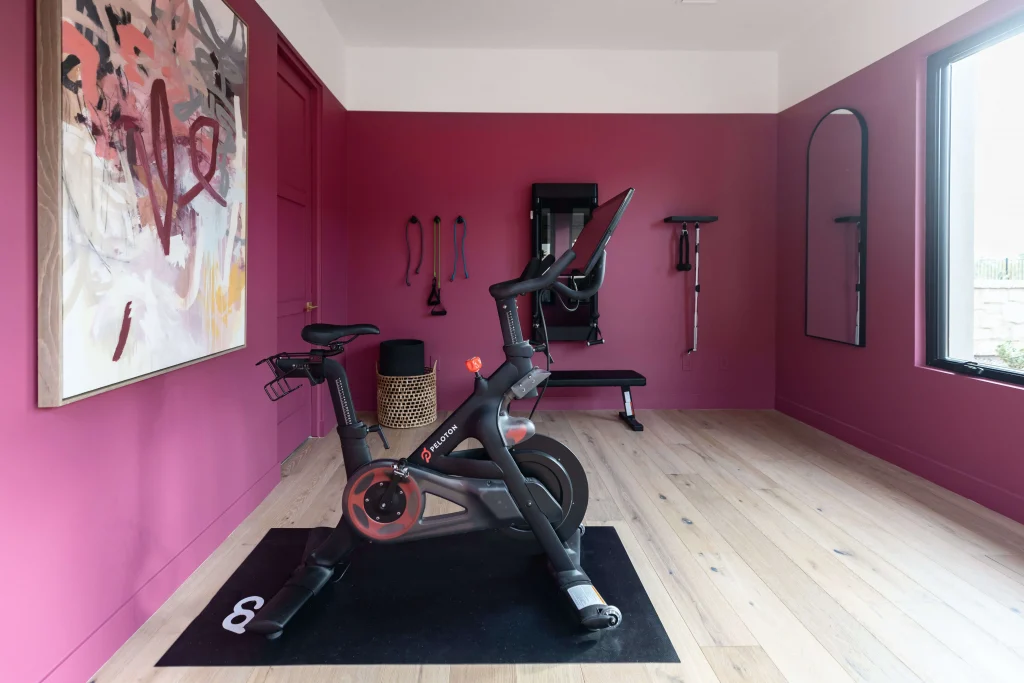 Home gym with bright pink walls, modern cycling equipment, and abstract artwork