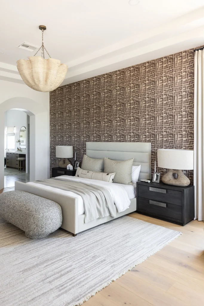 Neutral-toned bedroom with layered bedding, modern chandelier, and accent wallpaper