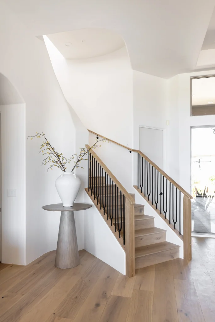 Curved staircase with wood railing and ceramic vase on pedestal