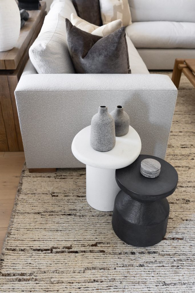 Two small tables, one white and one black, with gray vases are beside a light sofa with patterned pillows on a striped rug—Living with Lolo.