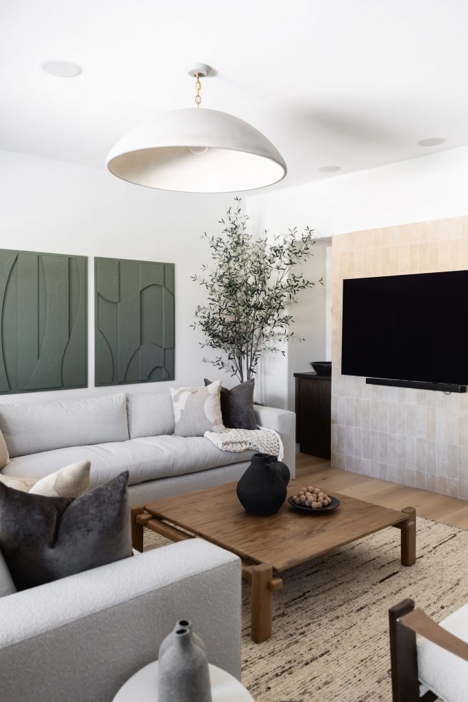 Modern living room with a white sectional sofa, wooden coffee table, wall-mounted TV, large green plant, and textured wall art—Living with Lolo.
