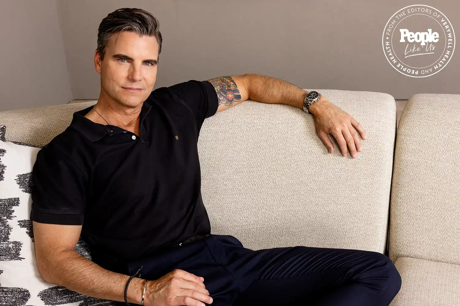 Actor Colin Egglesfield in black polo shirt relaxes on a beige sofa indoors. Actor Colin Egglesfield in black polo shirt relaxes on a beige sofa indoors