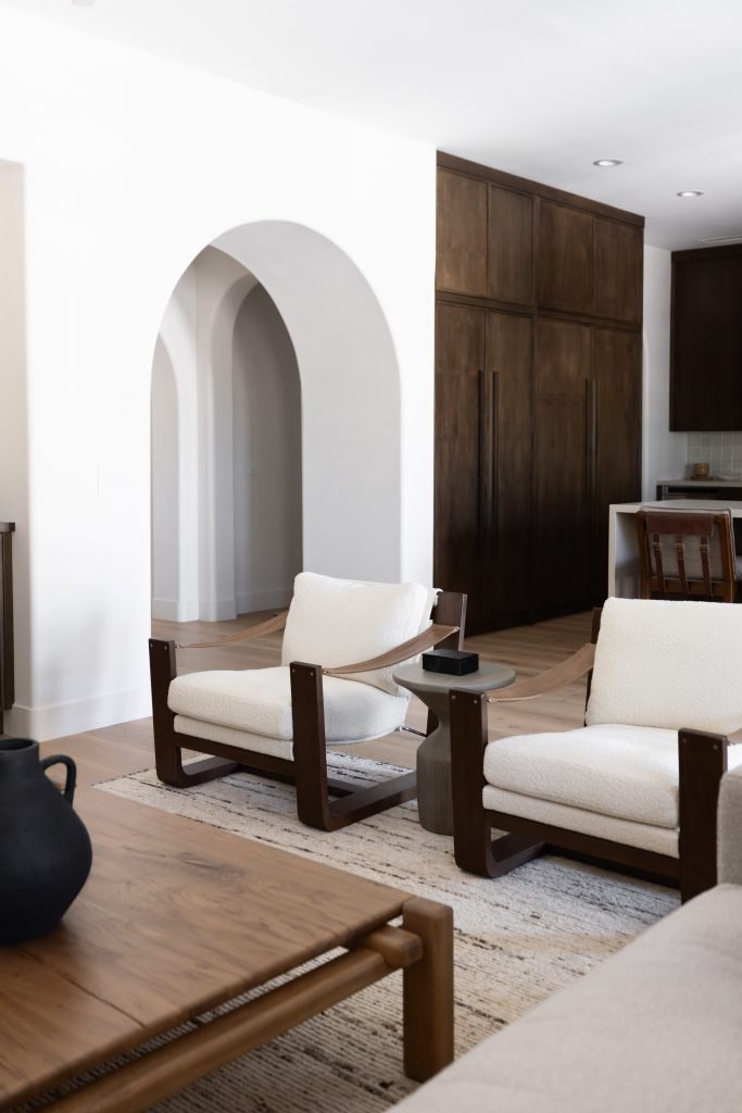 A living room with two white cushioned chairs, a wooden coffee table, neutral rug, dark wood cabinetry, and an arched doorway. — Living with Lolo.