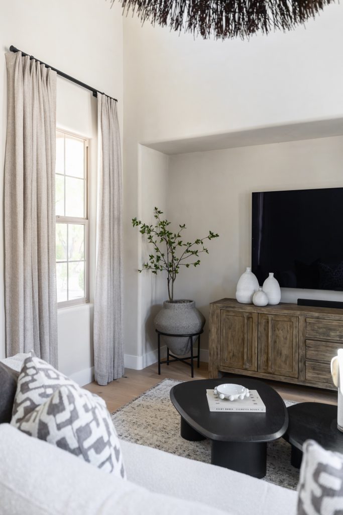 A modern living room with a wooden console, large TV, neutral decor, potted plant, light curtains, and a sofa with patterned pillows — Living with Lolo.