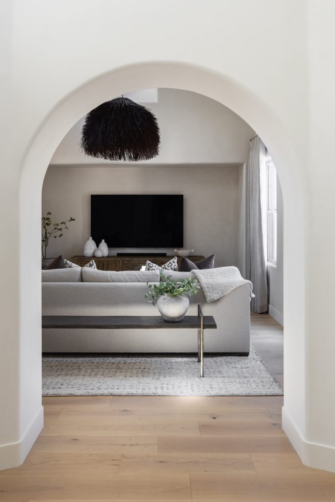 Modern living room with a grey sofa, patterned rug, TV, and black feathered ceiling light. Natural light from a right-side window—Living with Lolo.