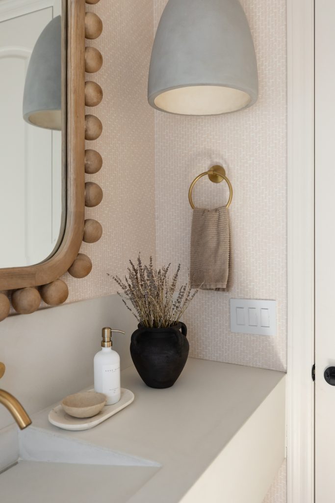 A bathroom countertop with a black vase, soap dispenser, dish, and beige towel on a gold ring below a pendant light. — Living with Lolo.