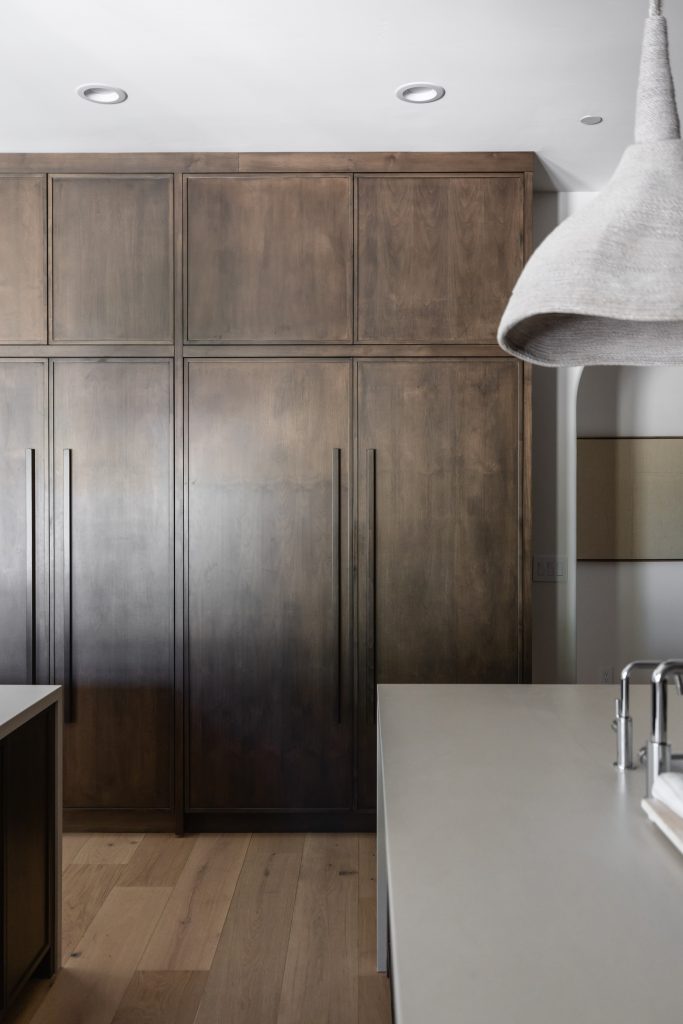 Modern kitchen with tall wooden cabinets, built-in appliances, light wood floors, and a white countertop with a faucet—Living with Lolo.