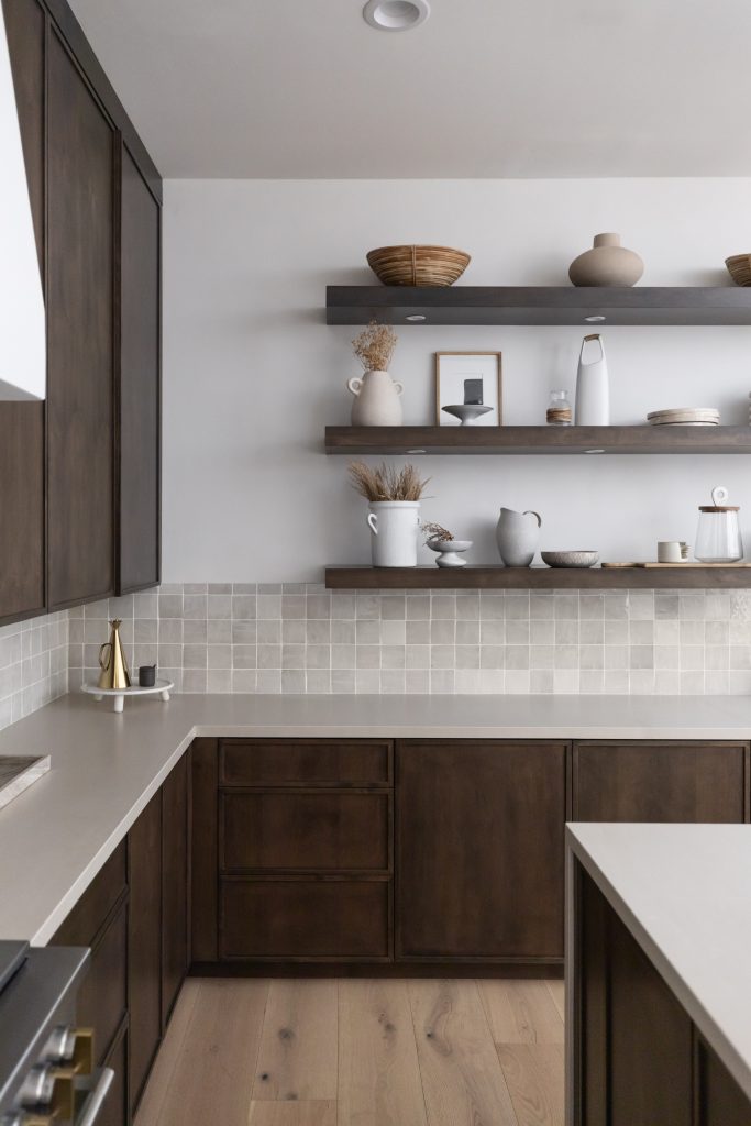 Modern kitchen with dark wood cabinets, light countertops, tile backsplash, and two wooden floating shelves on a white wall—Living with Lolo.
