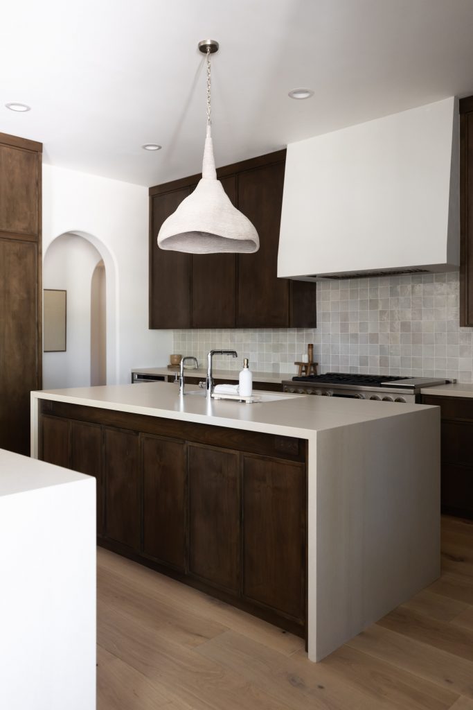 Modern kitchen with dark wood cabinets, white countertops, light wood floors, a large island with a sink, and a white pendant light—Living with Lolo.