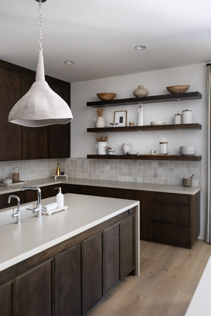 Modern kitchen with dark wood cabinets, white countertops, light wood floors, open shelves with dishes, and a large pendant light above the island — Living with Lolo.
