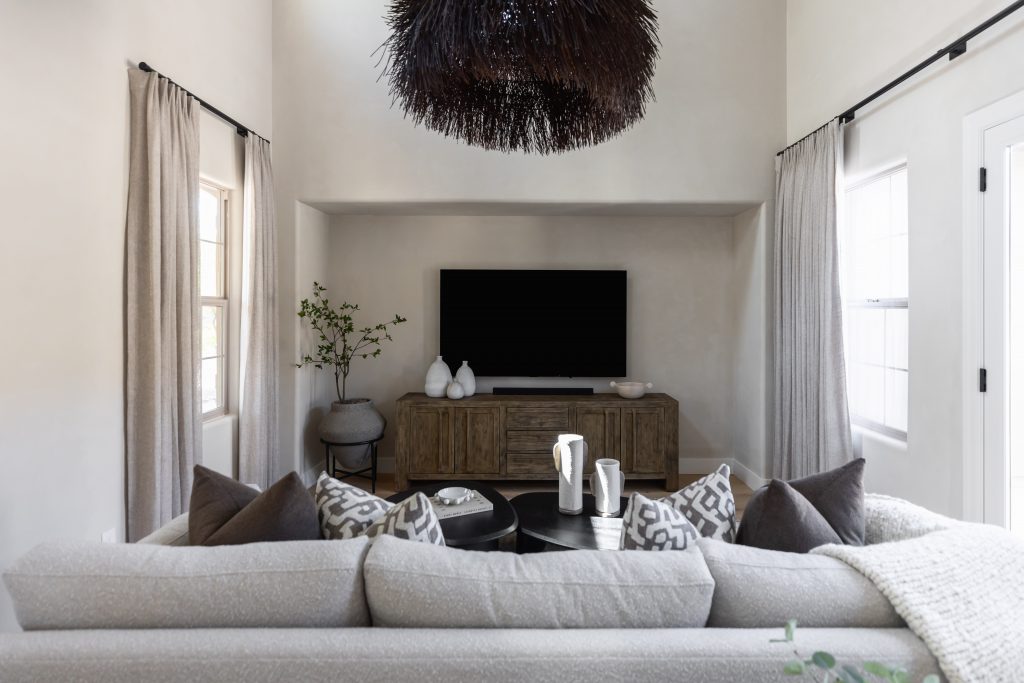 A light grey sofa, patterned cushions, wooden TV console, vases, round coffee table, neutral curtains, and black chandelier. — Living with Lolo.