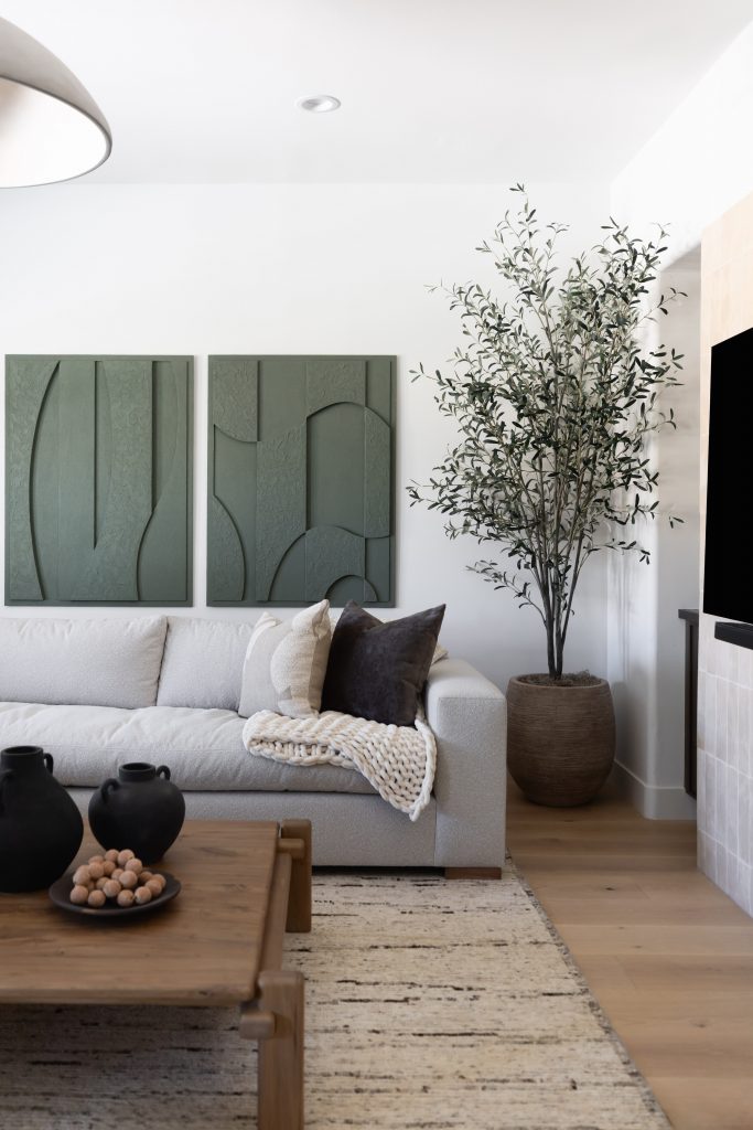A modern living room with a light sofa, dark pillows, textured blanket, wood coffee table, green wall art, and large potted plant. — Living with Lolo.