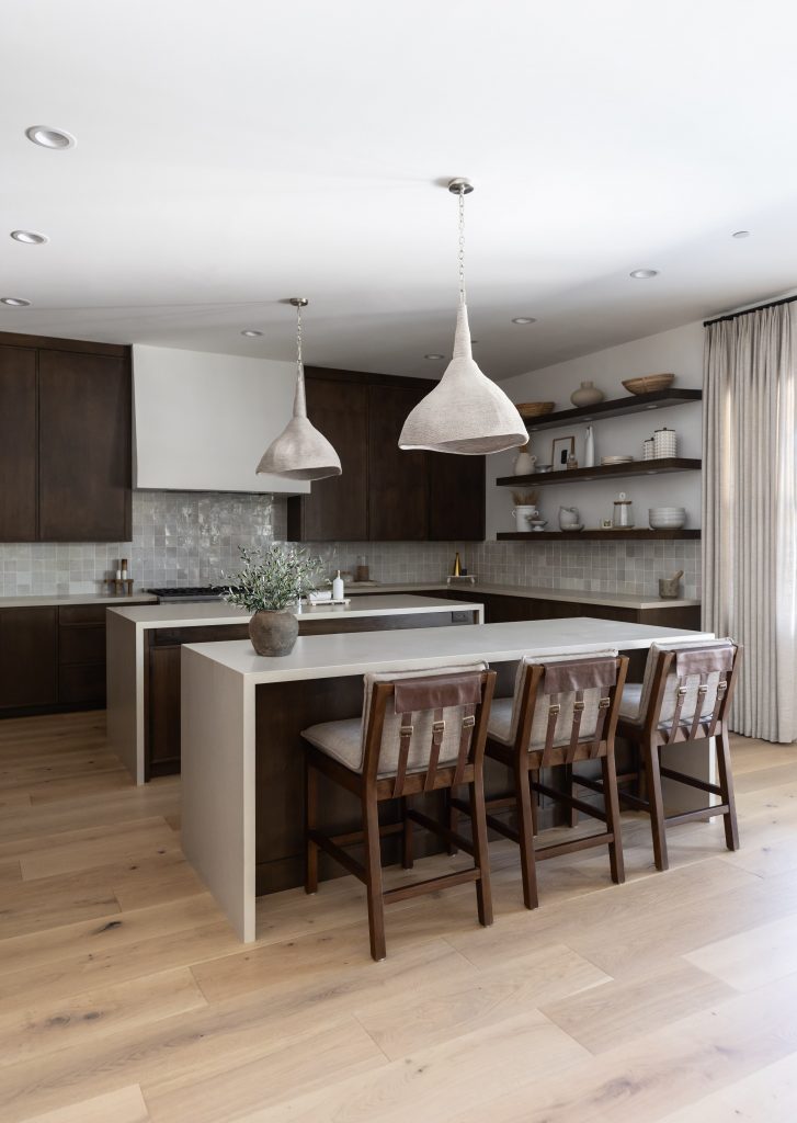Modern kitchen with a large island, three wooden chairs, dark cabinets, open shelves, light tile backsplash, and two pendant lights—Living with Lolo.